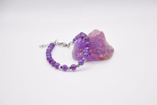 Bracciale in ametista poggiato su pietra grezza di ametista.