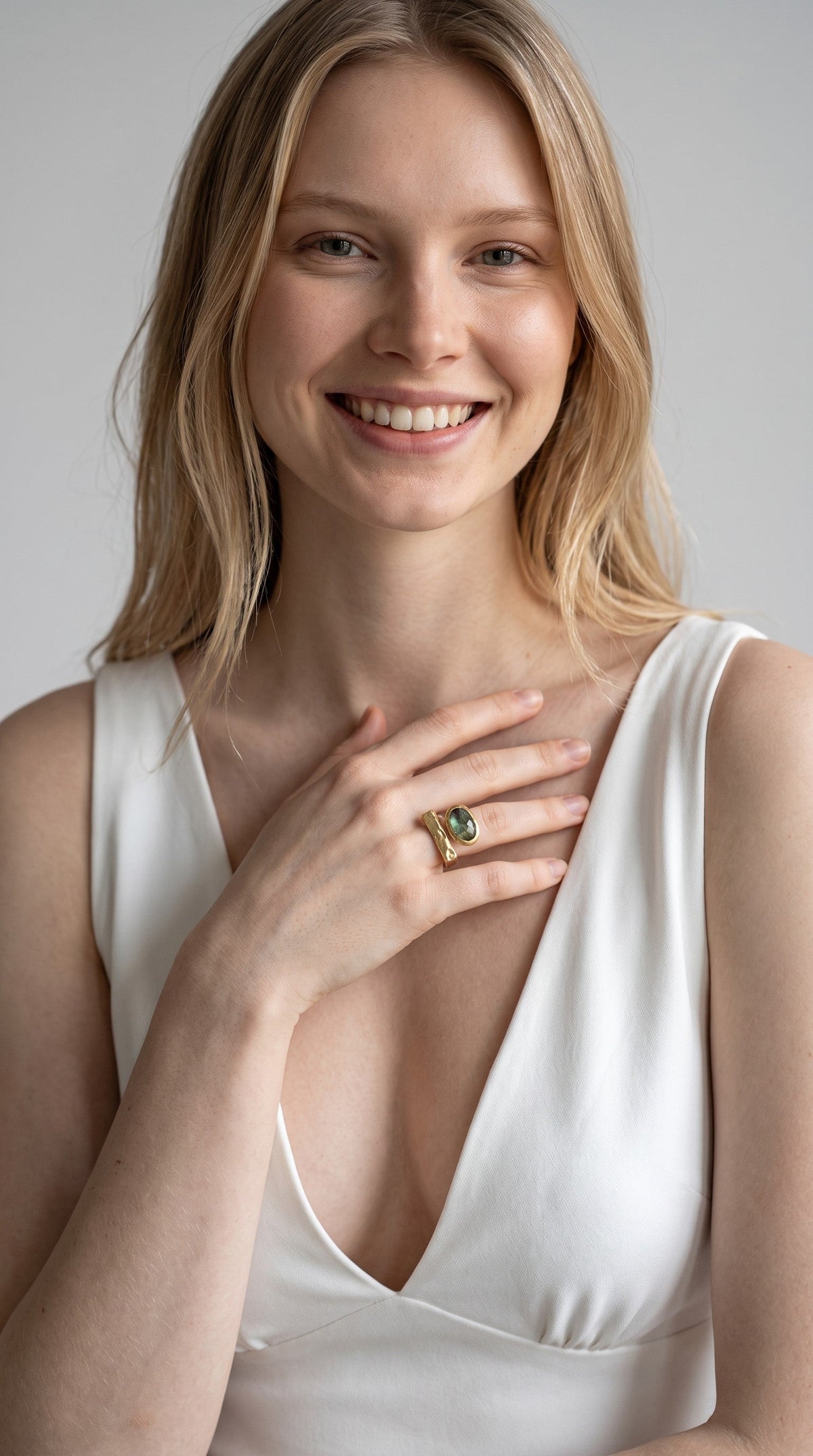 Modella sorridente indossa l'anello DSCREAZIONI Frammento Smeraldo in bronzo dorato 18k con pietra ovale sfaccettata